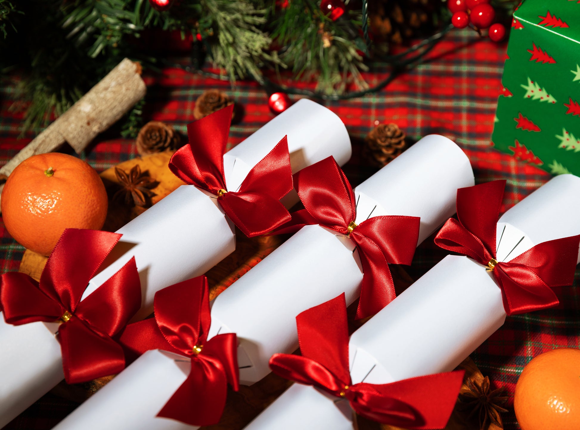 Decorative Bad Crackers Christmas crackers with red ribbons on a festive background with oranges and a tree.